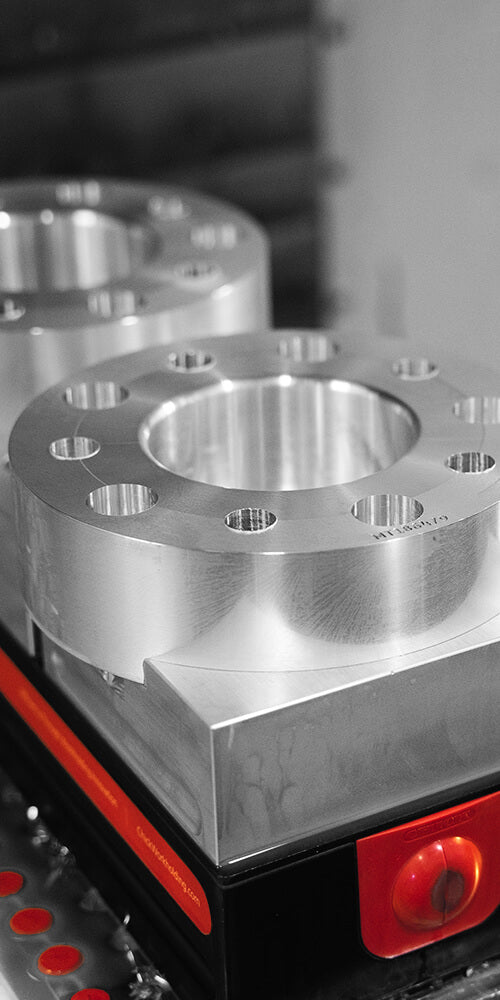Close-up of shiny, cylindrical metal parts with multiple holes, set on a machine.
